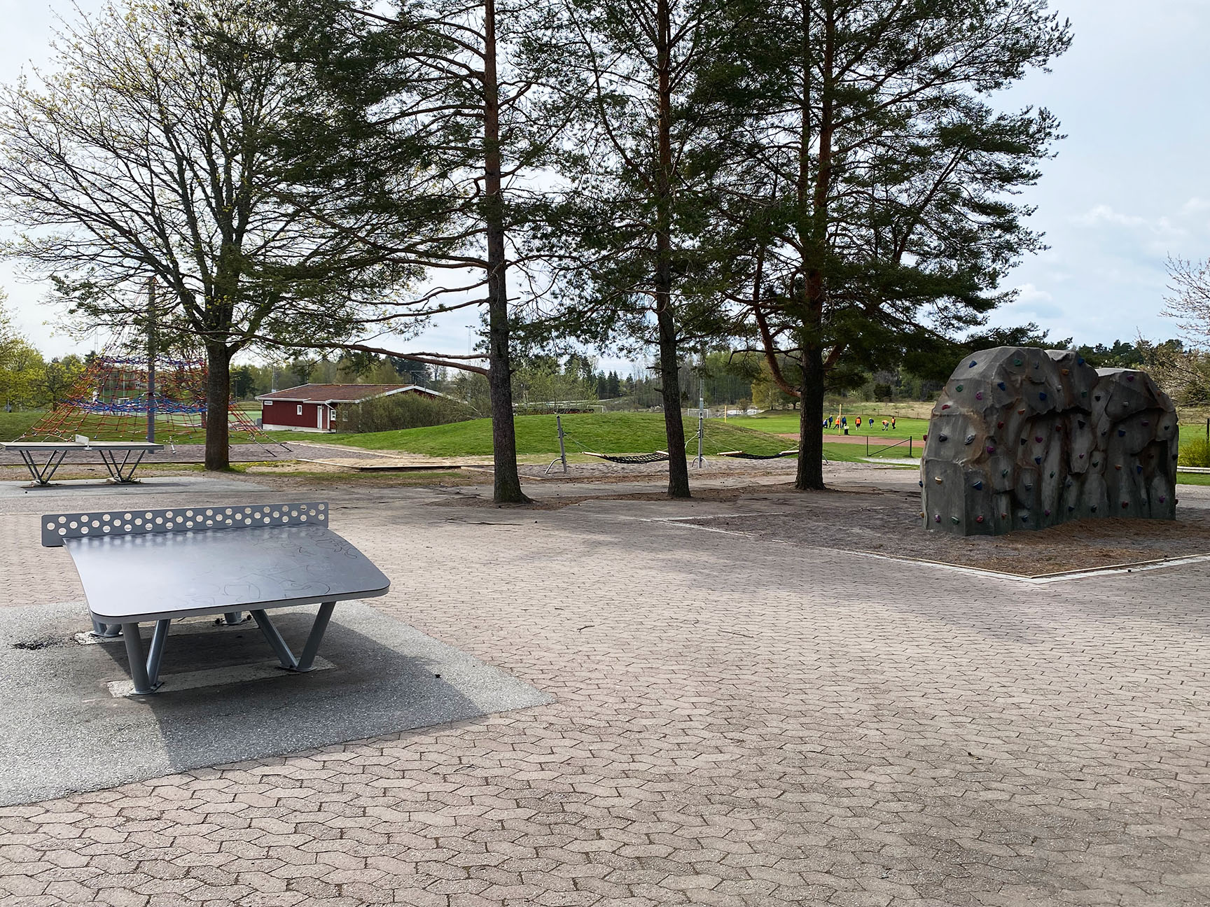 En skolegård med multispillbord, klatrestein og en klatrepyramide i bakgrunnen.