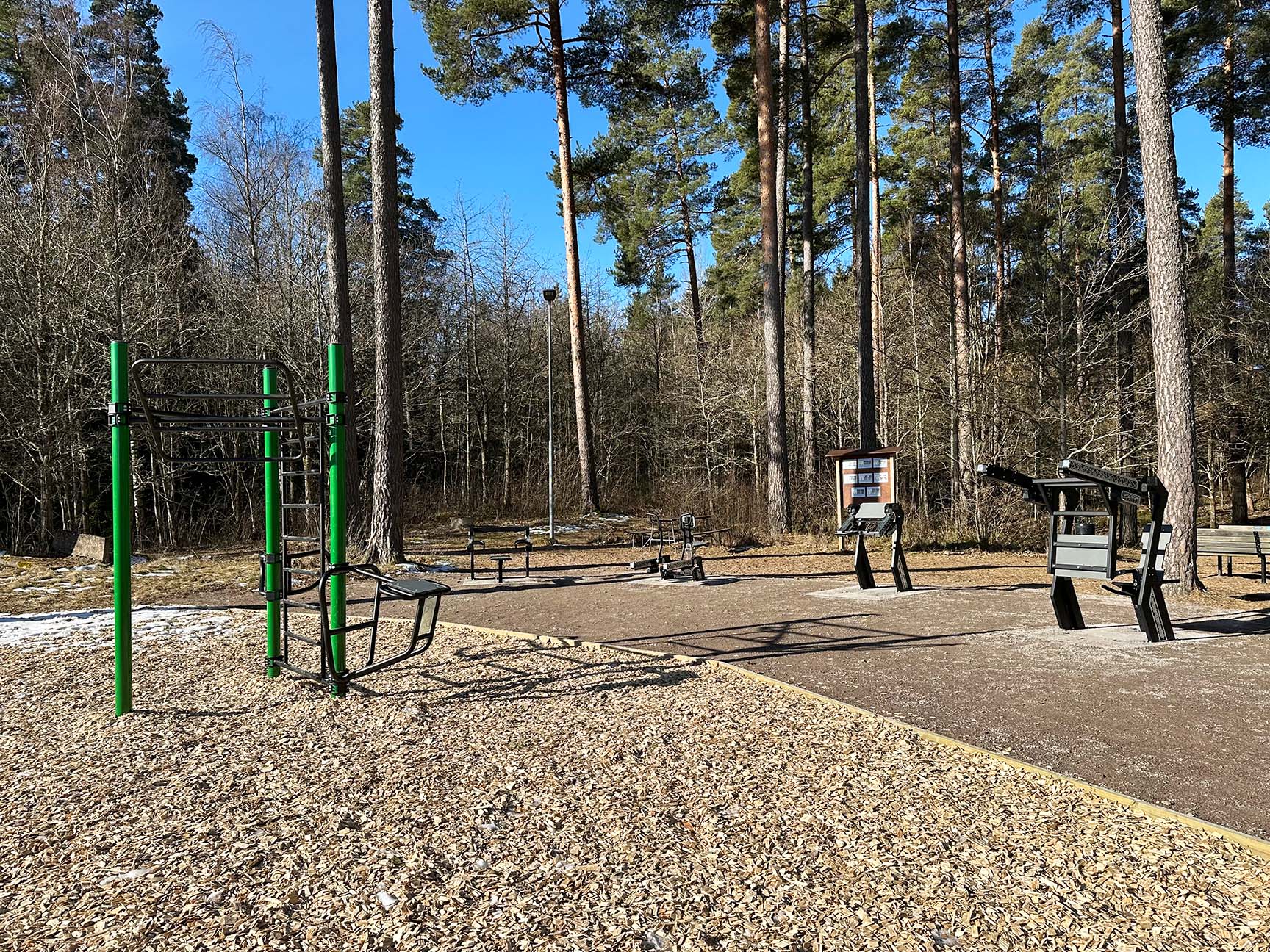 Grønn treningsstasjon og svarte treningsapparater i en park 