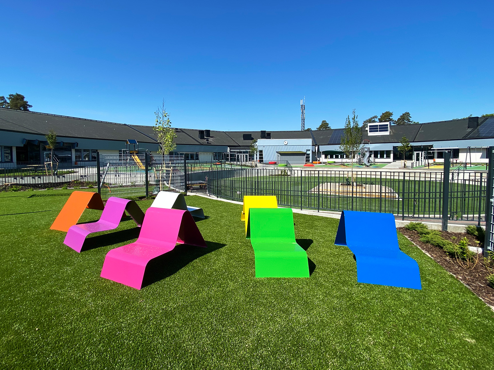Fargerik skolegård med trampoline, sklie og klatrestativ.