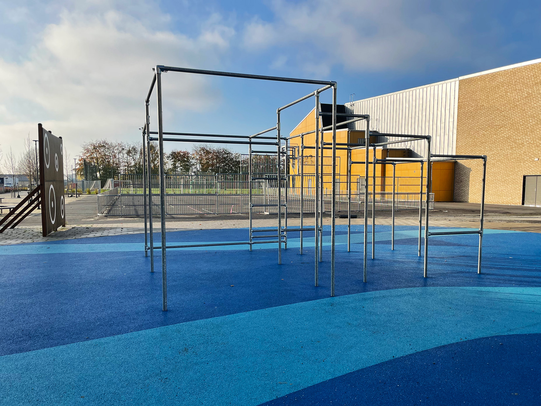 Parkourstativ på blått underlag, med ballvegg og multibane i bakgrunnen