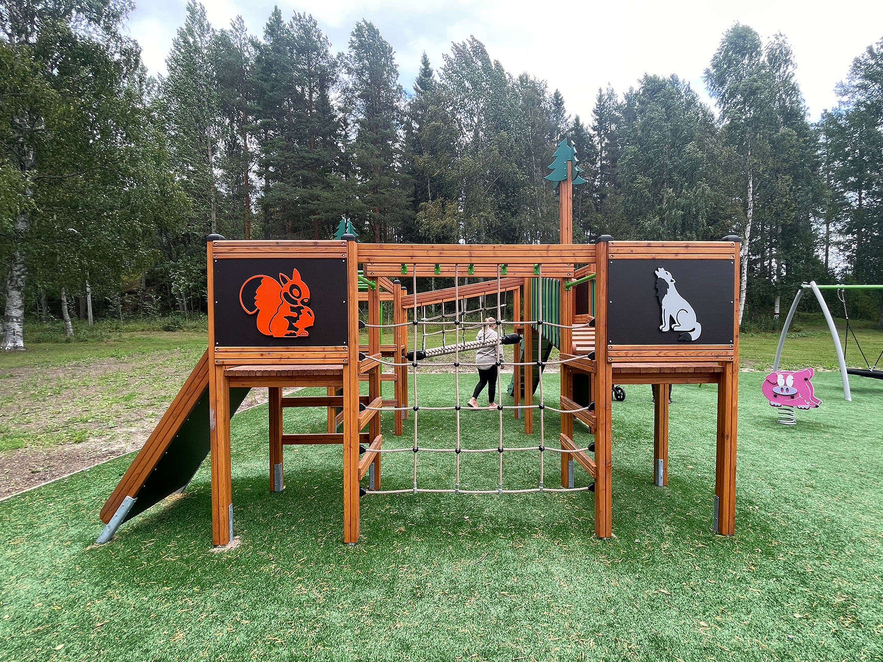 Lekeapparat med villmarkstema, omgitt av grønt gress og parkmiljø