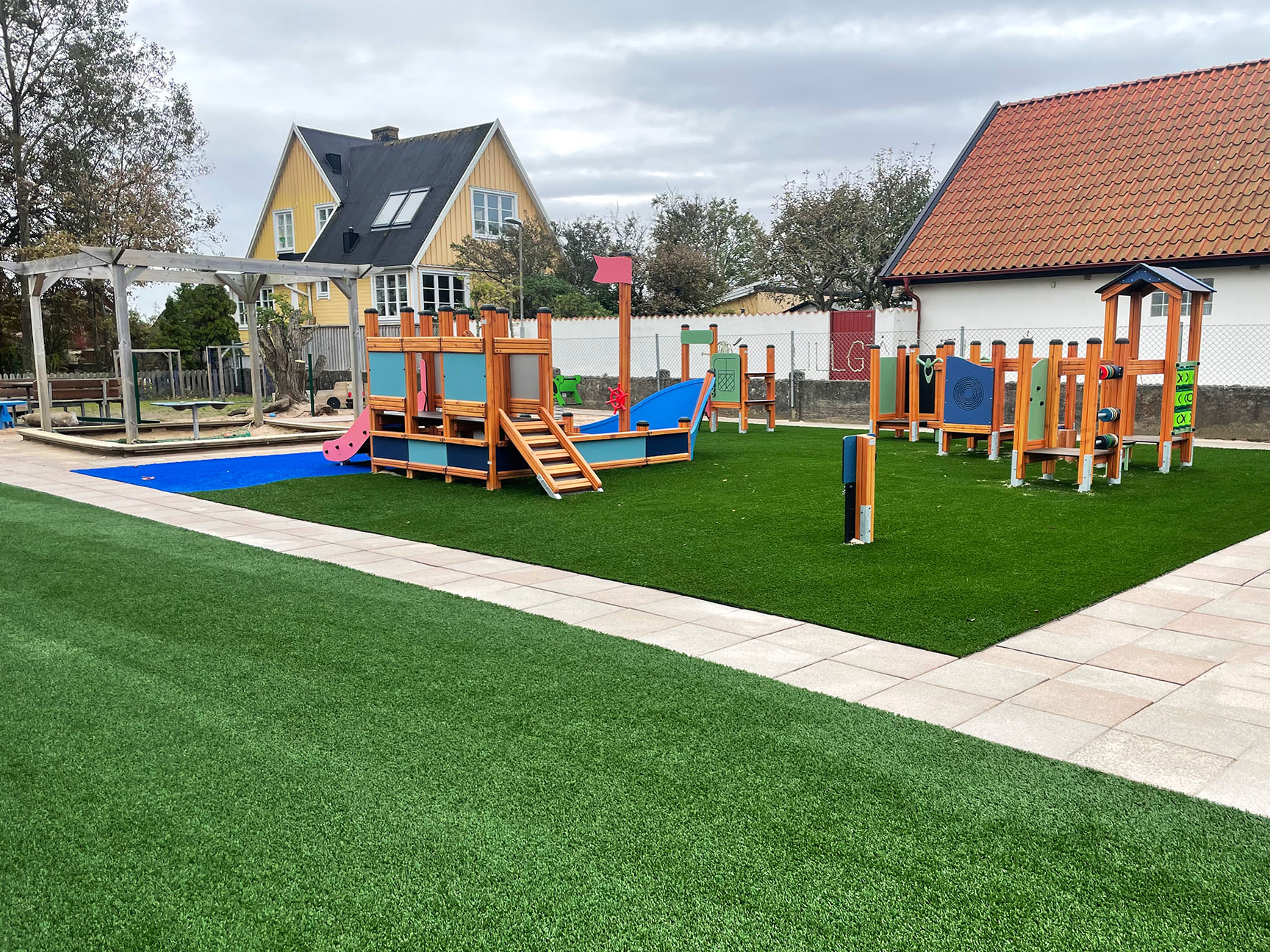 Lekeplass med klatrestativ og balanseløype på grønt og blått kunstgress