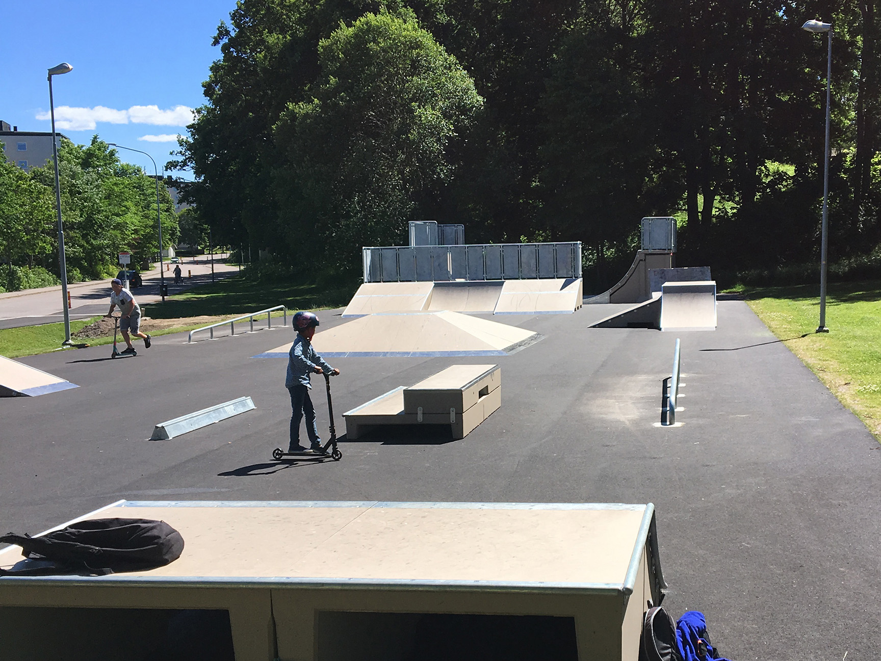 Skatepark med barn som kjører sparkesykkel og skateboard.