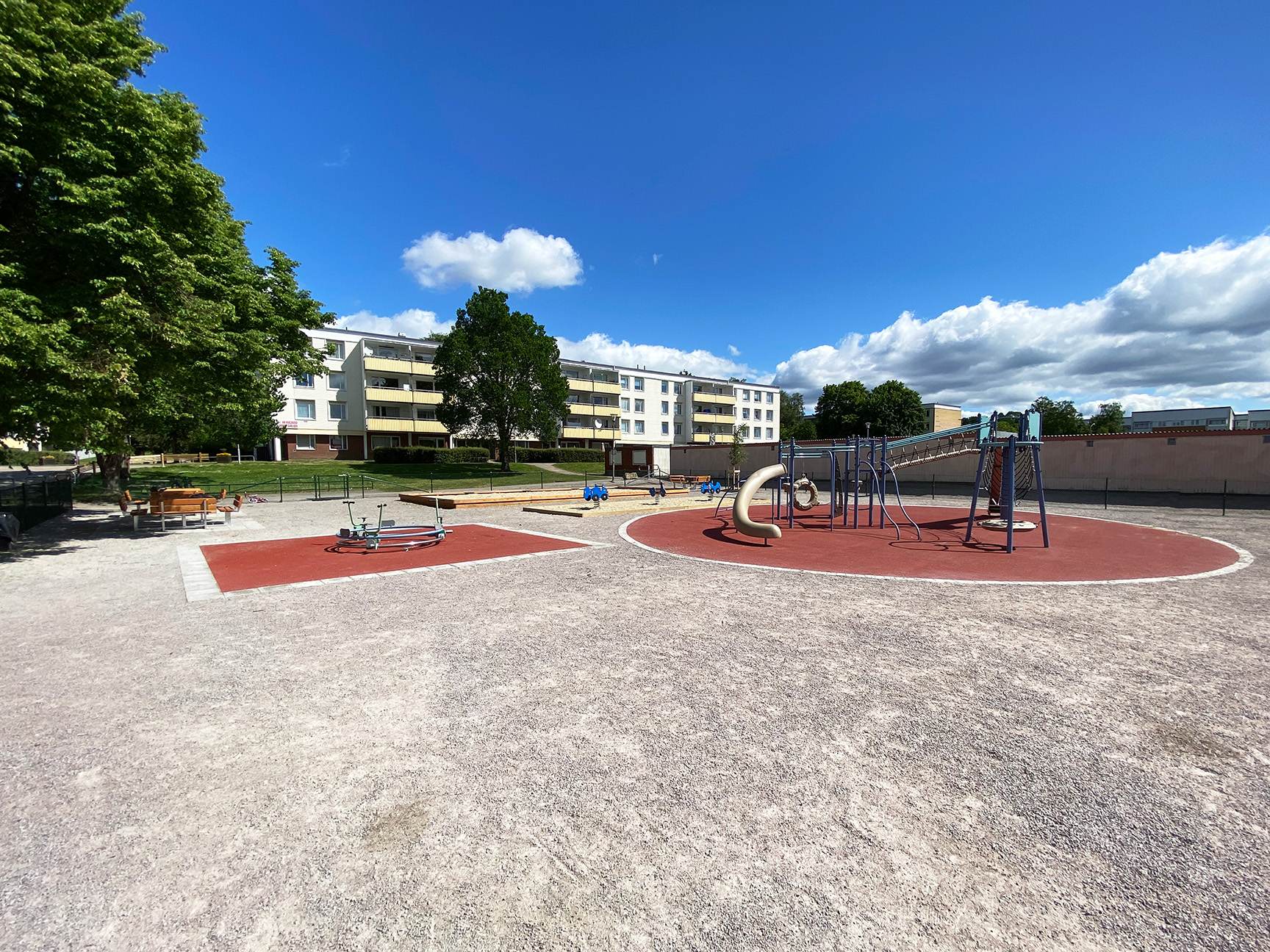 Lekeplass med klatrestativ og karusell på grusområdet ved borettslaget.