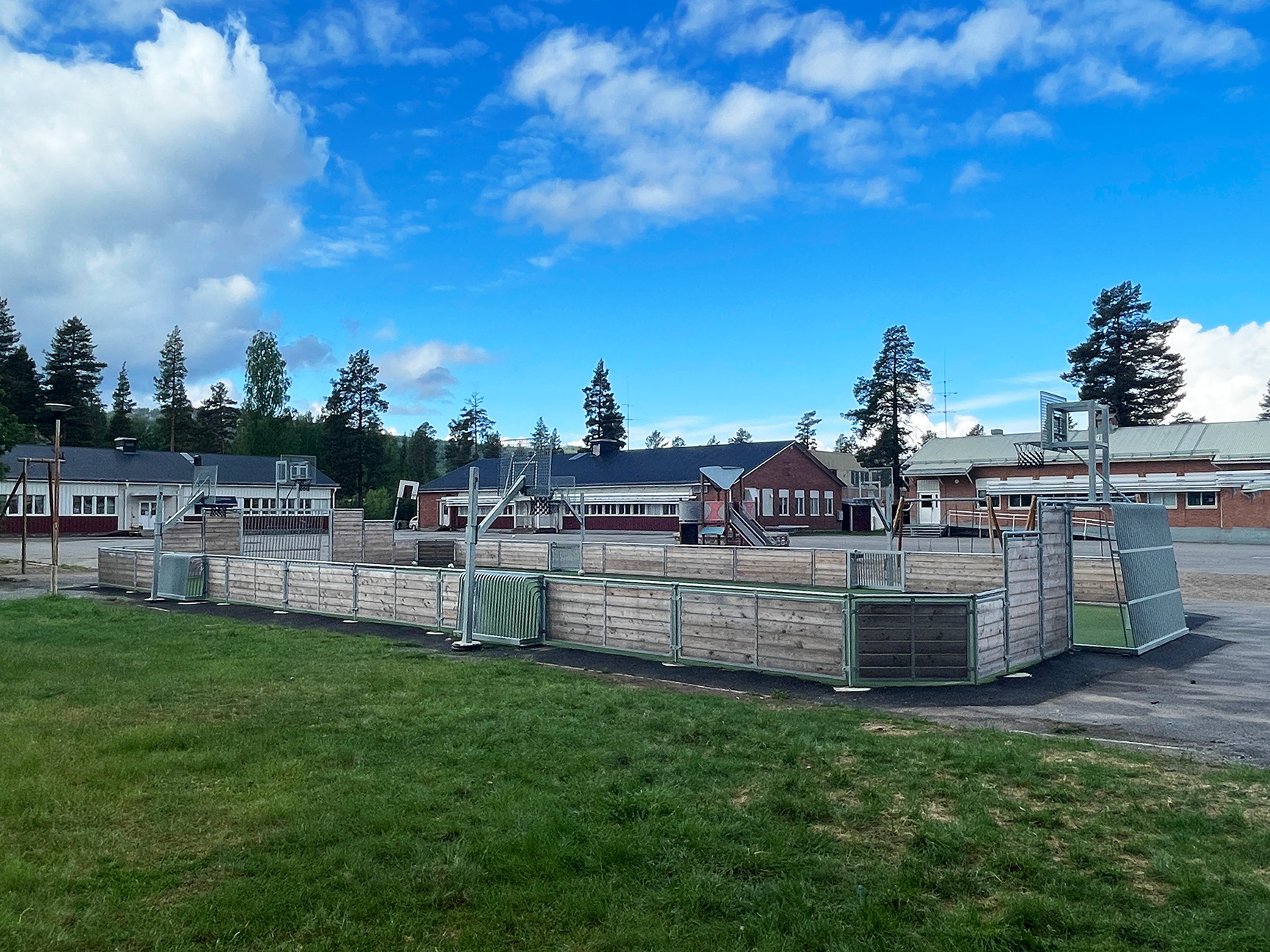 Ballbinge i tre med basketballstativ, arenamål og kunstgress – perfekt plassert på en skolegård.